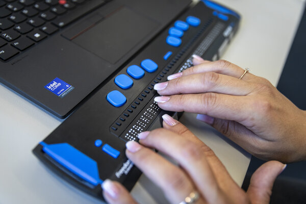 Nahaufnahme: Hände lesen Text mit einer Braillezeile am Computer.